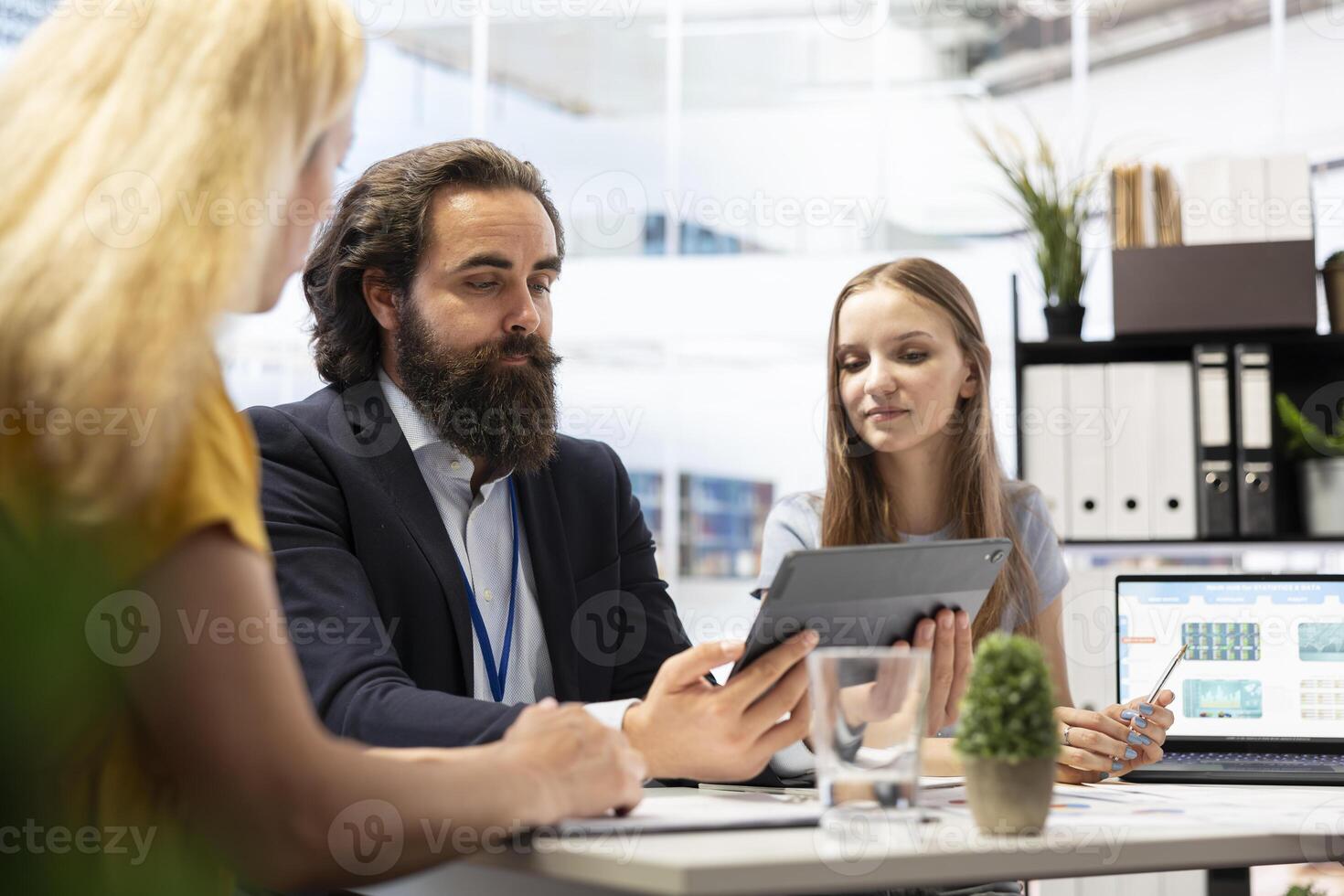 Counselor showing people financial plan on tablet, helping them fulfill economic goals and make money. Advisor teaching clients how to improve financial situation and increase income using device photo