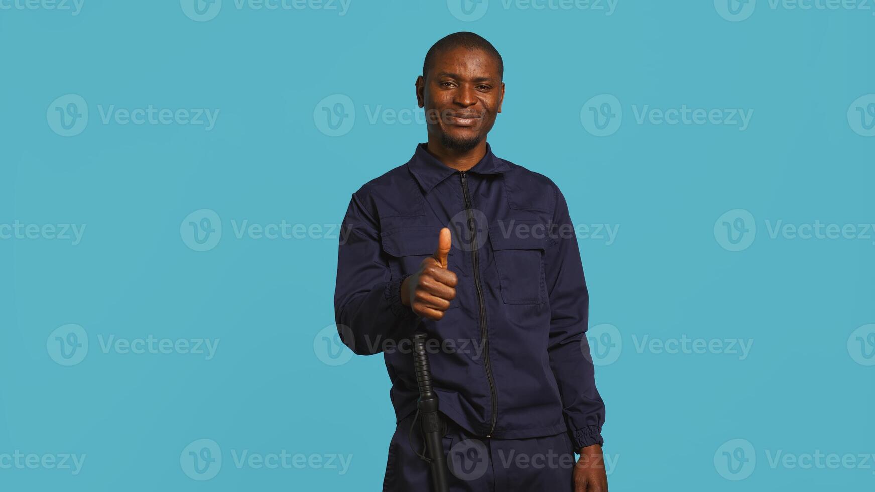 Happy security guard doing thumbs up sign gesturing with finger, preventing public access in restricted area. Portrait of smiling bodyguard doing positive hand gesture, studio background, camera B photo