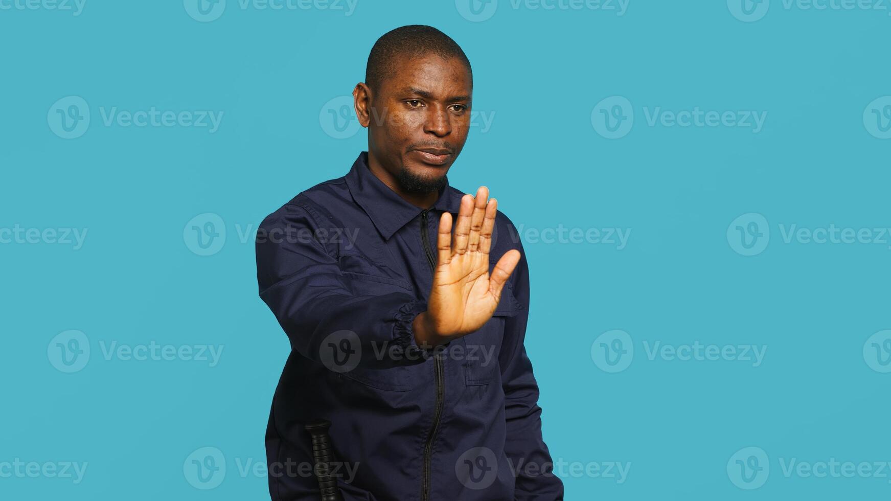 Portrait of security guard doing stop sign gesturing to intruder while overseeing premises. Private law enforcement worker showing halt hand gesture to trespasser, studio backdrop, camera A photo