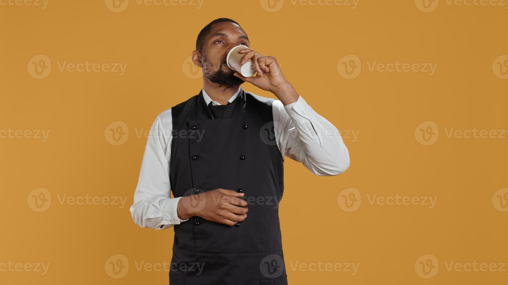 Restaurant waiter enjoying a cup of coffee drink on his work break, relaxing with caffeine beverage while on duty. Employee works in customer service hospitality industry, professionalism. Camera B. photo