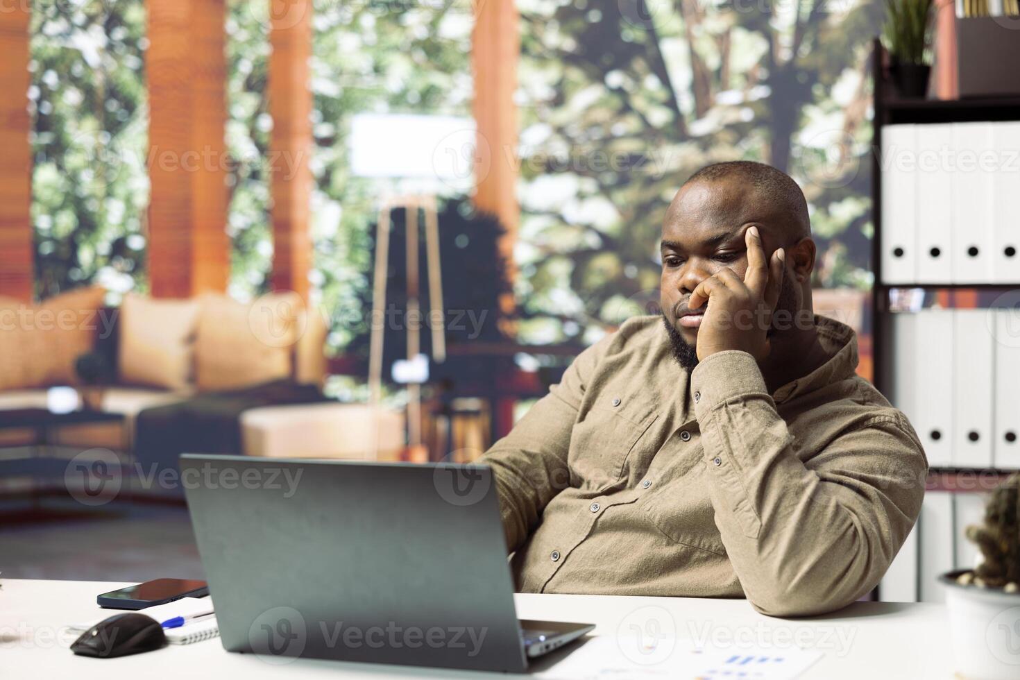 Startup administrator thinking of ways to increase business profit and funds, using a laptop to manage online marketing and social media strategies for his home based enterprise. Remote work. photo