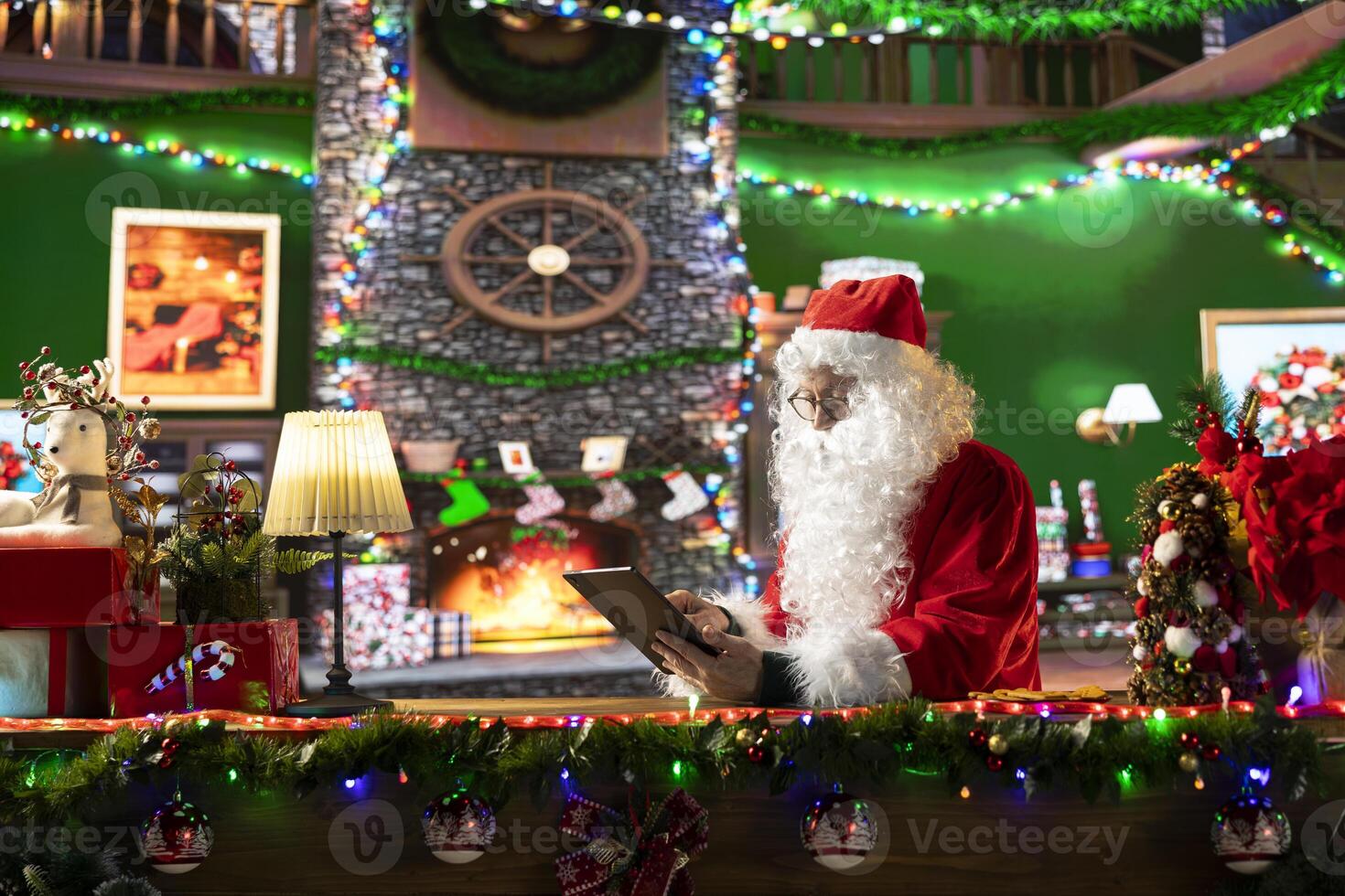 Father Christmas checking his online gift lists on a tablet in his cozy festive cabin. Man at the North Pole is connected to the world through the internet, bringing Christmas magic to life. photo
