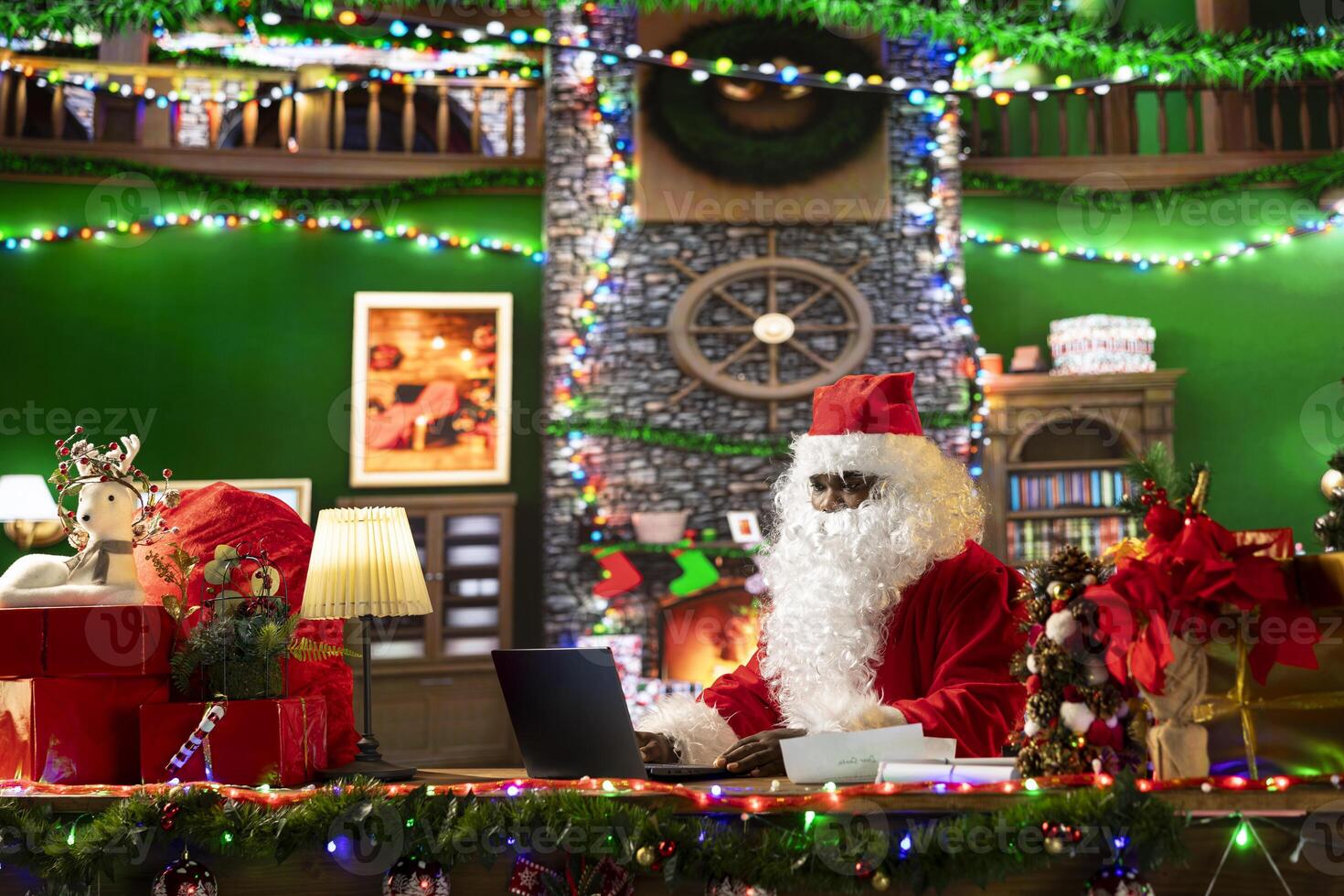 Santa Claus searches online for gift locations using his laptop in a festively decorated cabin at the North Pole. Saint Nicholas is connected to the world, making Christmas magic happen. photo
