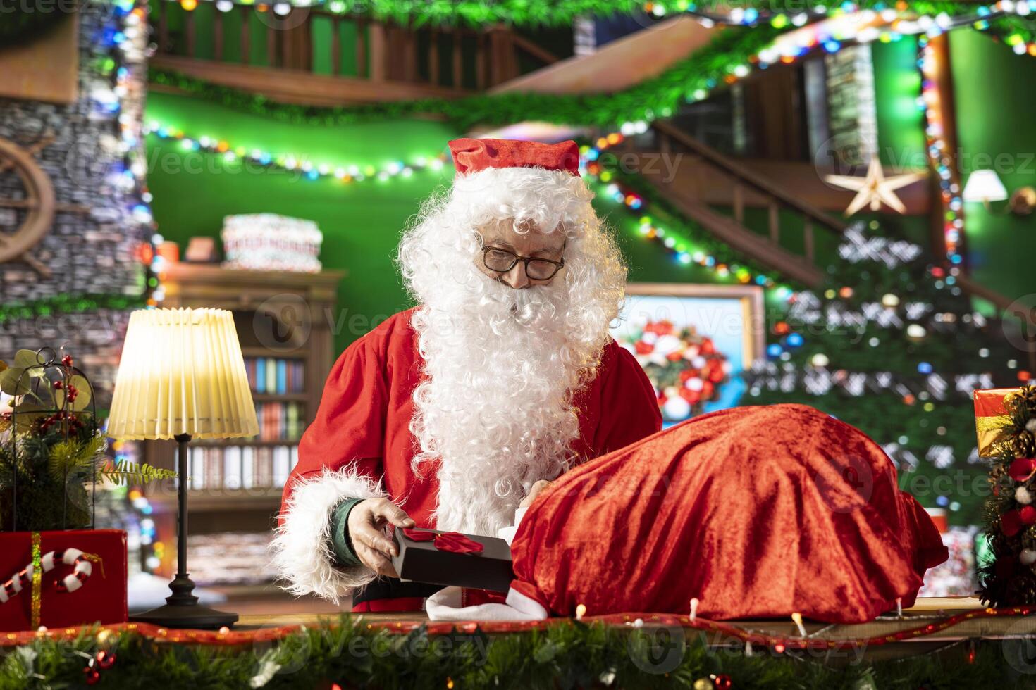 Saint Nicholas carefully wraps a gift in his North Pole workshop. The festive lights, decorations and magic of the holiday season fills the scene as Santa Claus prepares gifts to spread x mas joy. photo