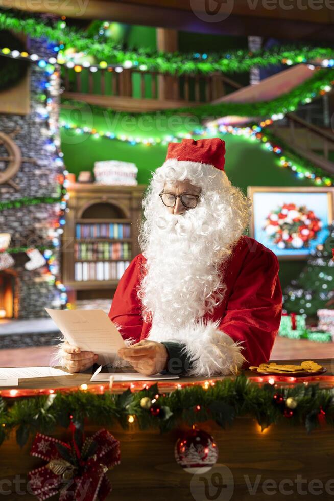 Father Christmas reading a wish list from children in his North Pole log cabin. Postcards of dreams and toys warm the holiday spirit in traditional Christmas scene, checks who is naughty or nice. photo