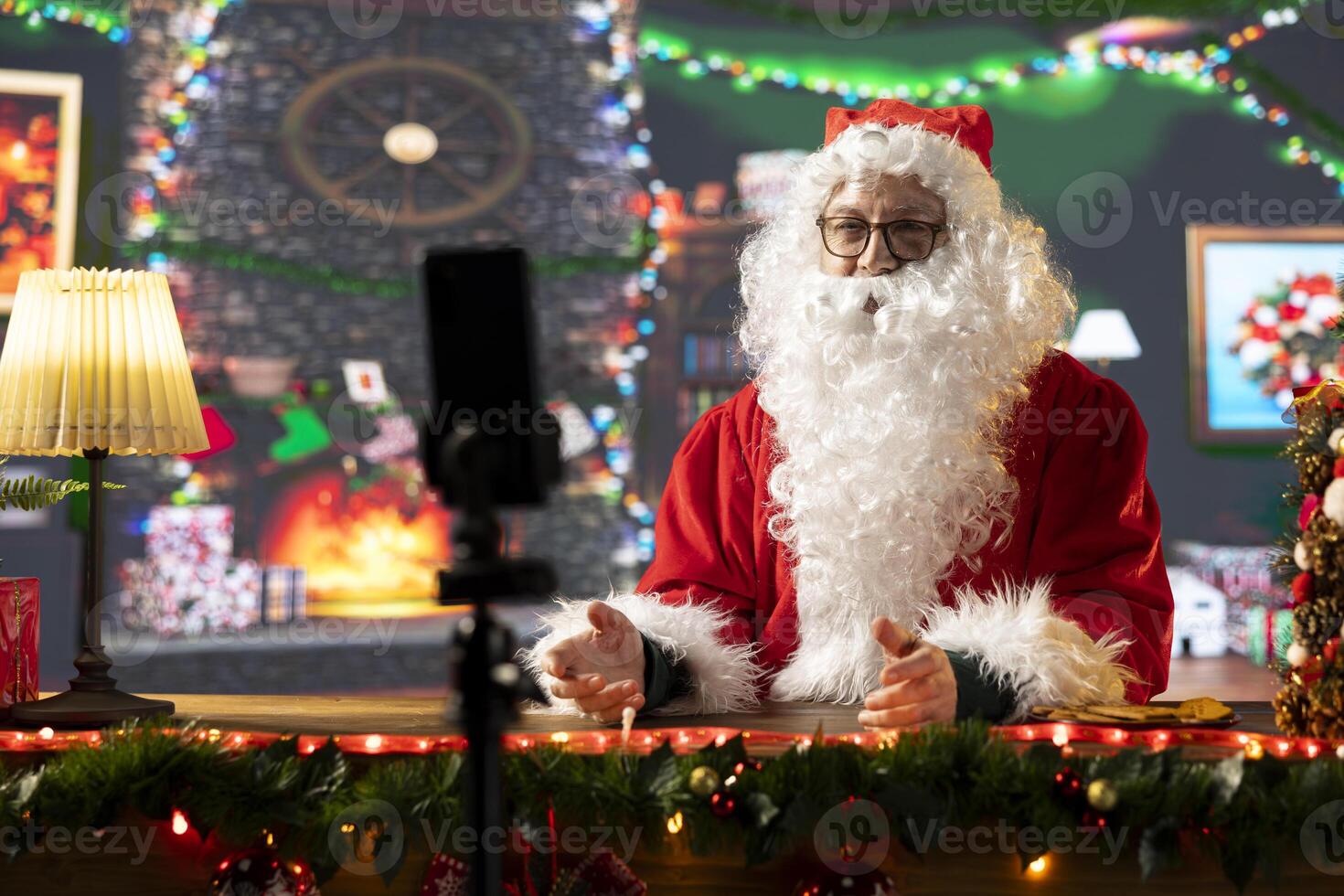 Father Christmas records a vlog talking to his online audience about the magic of Christmas. Santa Claus in a cozy festive cabin connects with subscribers through social media during wintertime. photo