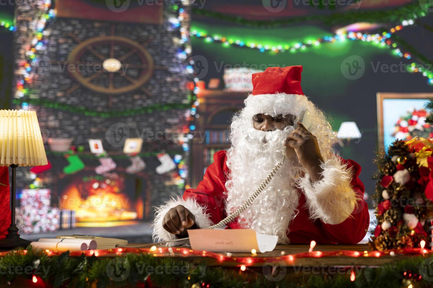 Santa Claus reading letters and calling helpers on landline phone call, in his festive decorated North Pole. Spreading holiday cheer with Christmas lights and decorations, magic of gift giving. photo