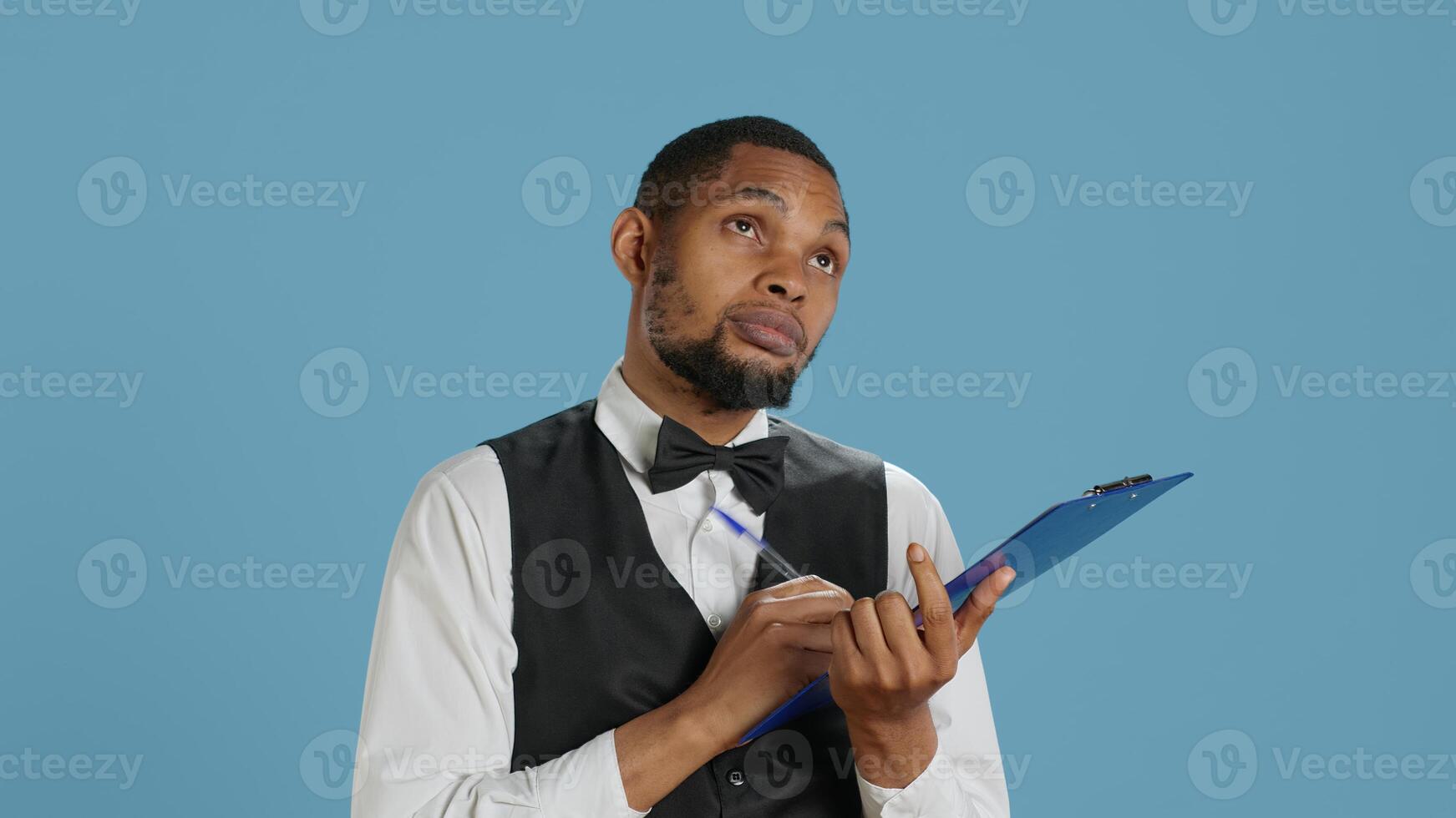 Receptionist worker writing down notes on clipboard files, ensuring easy check in process for hotel guests against blue background. Bellboy staff providing excellent concierge services. Camera A. photo