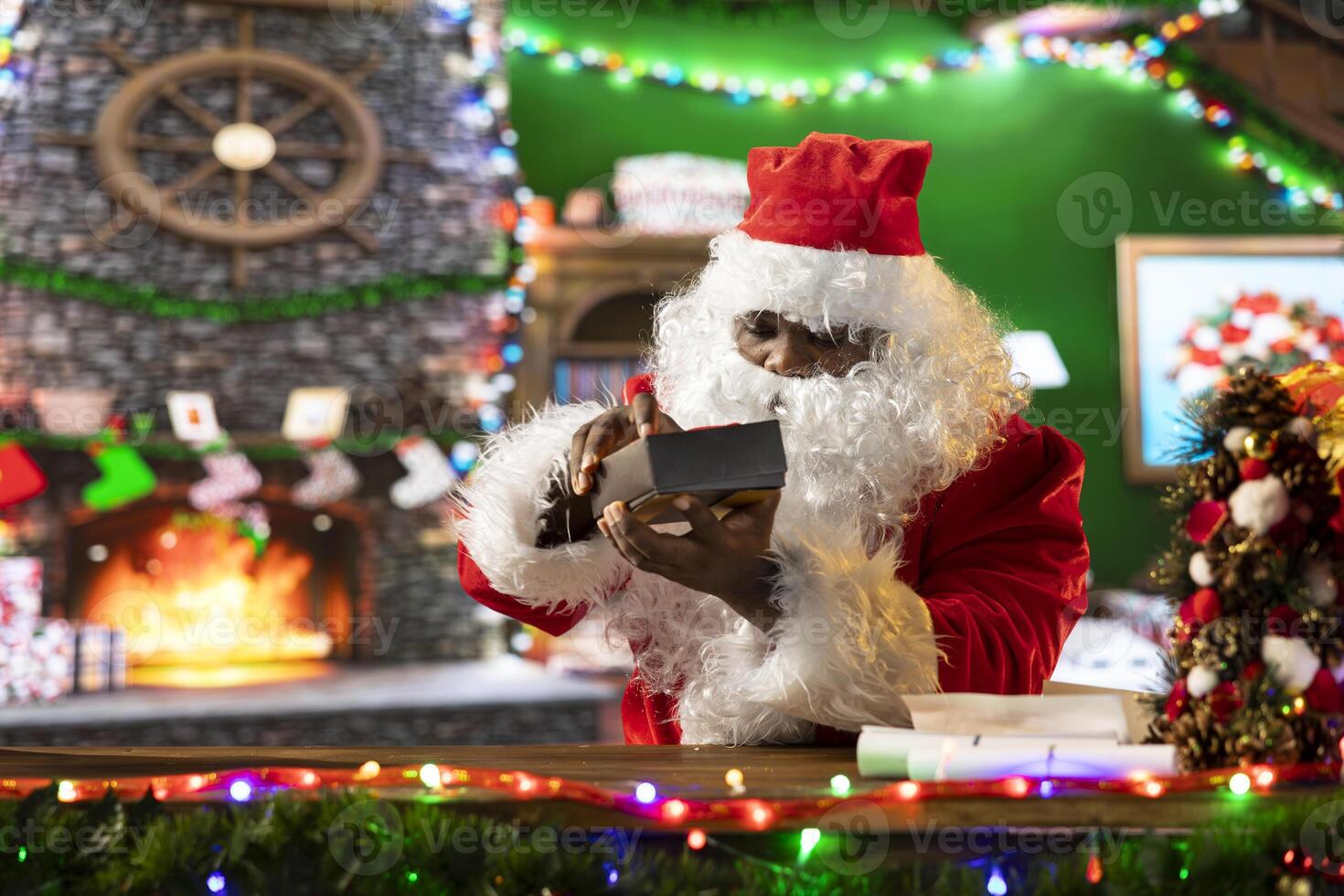 Father Christmas opening a gift box with a light shining bright in it, verifying all the presents before leaving on the Christmas eve journey. Black Santa checking the toys, holiday tradition. photo