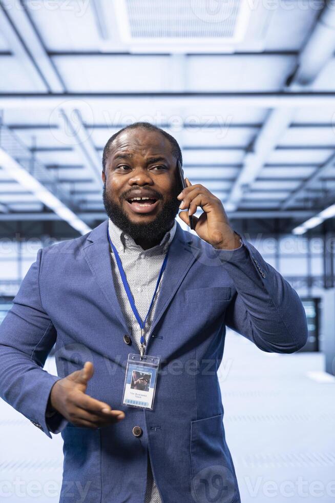 Manager talking on smartphone in high tech data center housing advanced computing gear. Specialist delegating tasks in technologically advanced server hub during telephone call photo