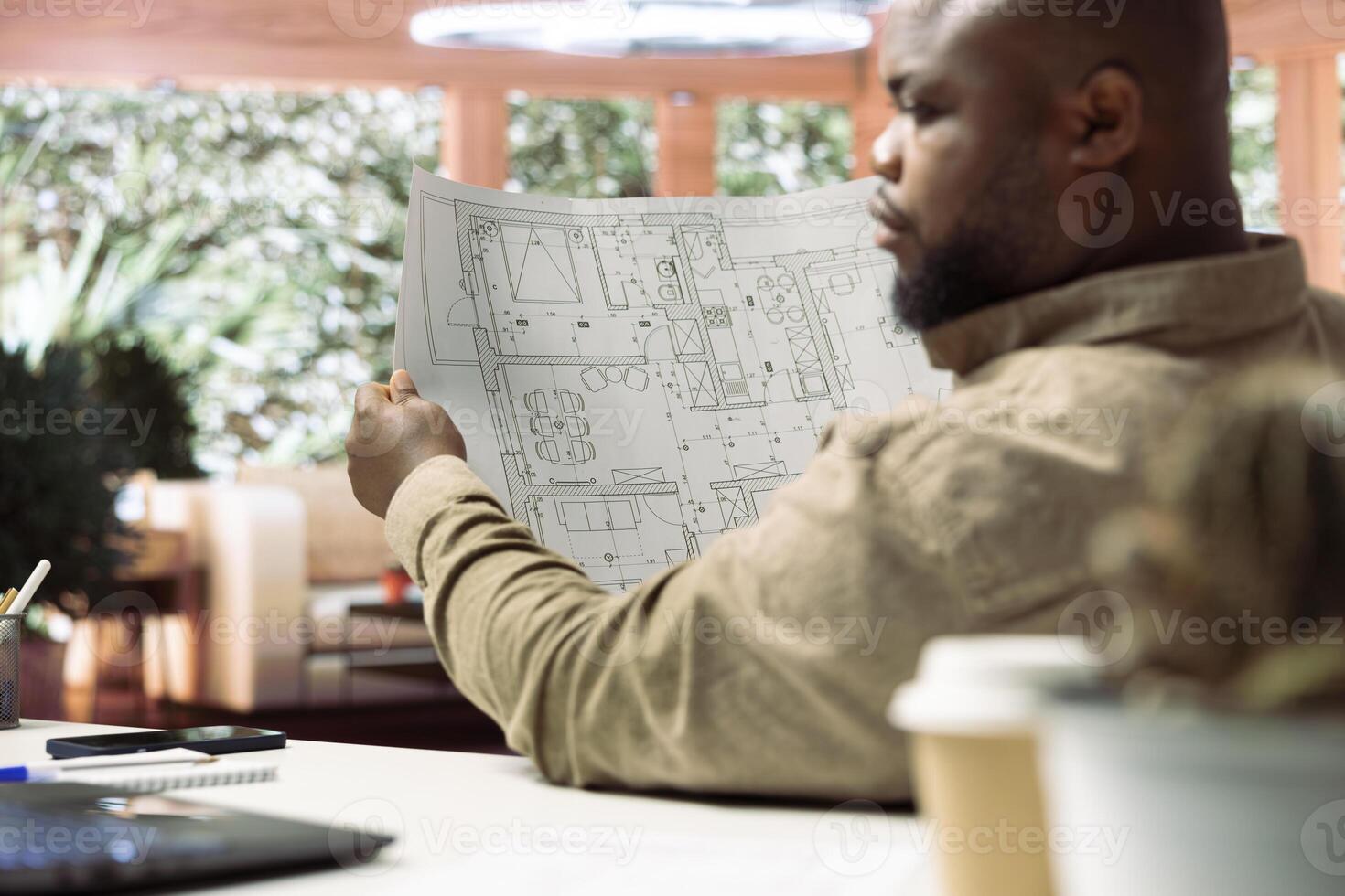 Businessman studying architectural blueprint plans at home office, using digital tools to review and plan office spaces for relocation. Business development strategy with property renting. photo