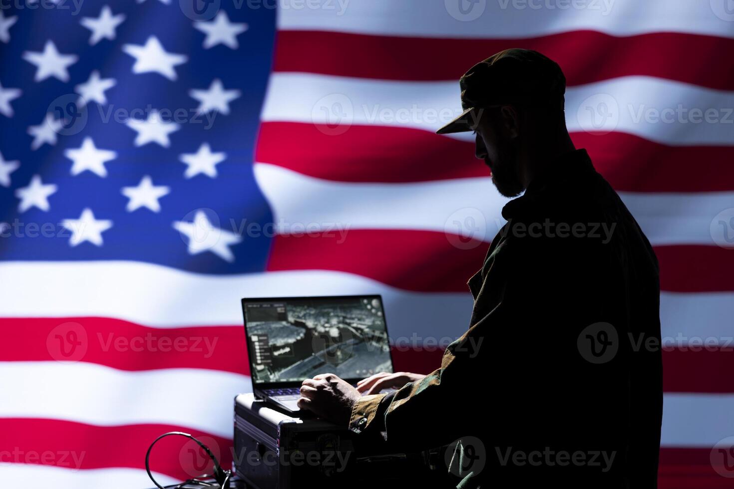 Military operative uses laptop to analyze surveillance data, standing isolated over USA flag background. Soldier engaged in geopolitical operation, protecting national borders photo