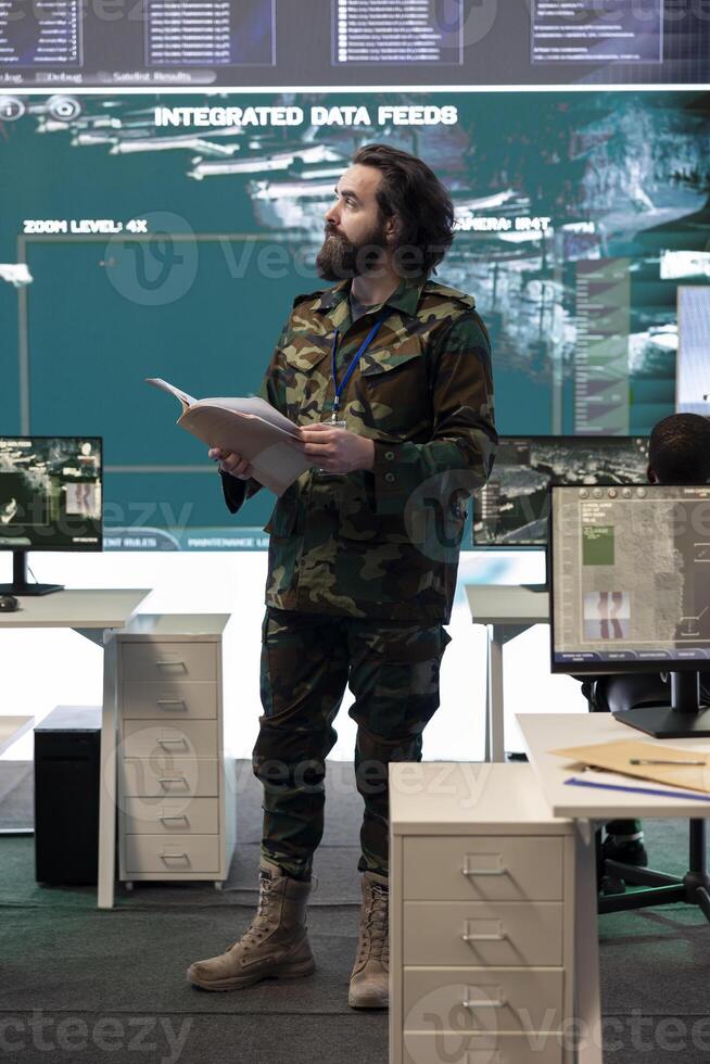 Military personnel examining live satellite imagery on a big screen in army base of operations, gathering intelligence for future national safety missions. Serviceman employs reconnaissance system. photo