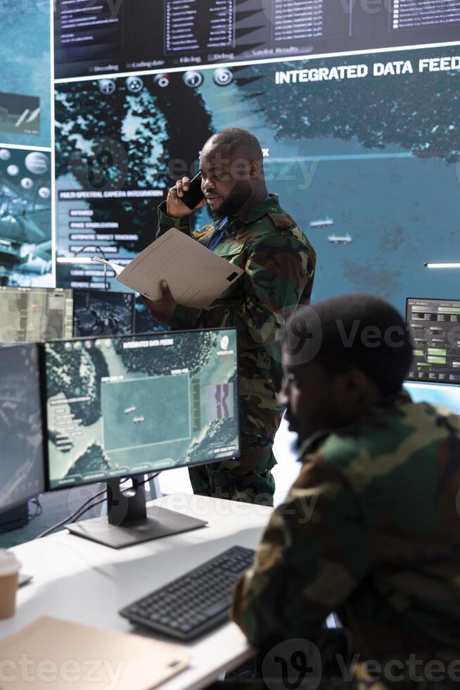 Army professional in command center talks on phone call and gives crucial information, overseeing satellite data in real time. Protect national security and support strategic military missions. photo