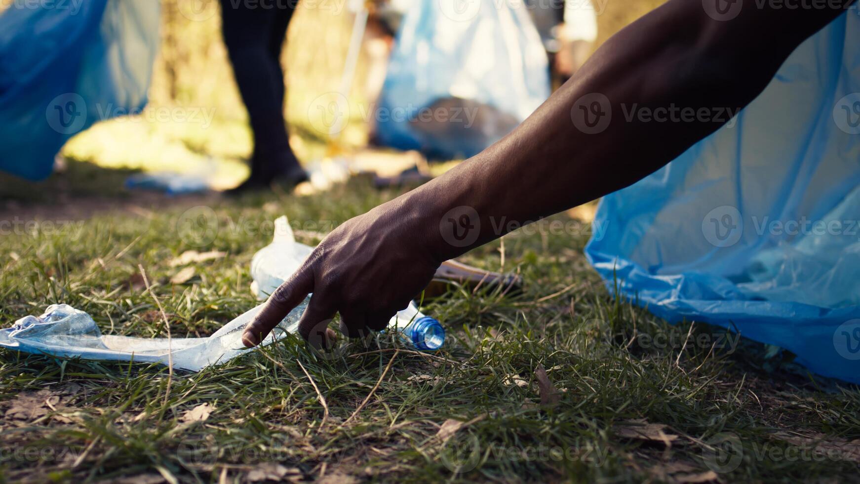 People supporting cleanup of the natural environment by grabbing recyclables and trash objects from the woods, collecting in a garbage bag. Using utensils to pick up rubbish. Close up. Camera B. photo