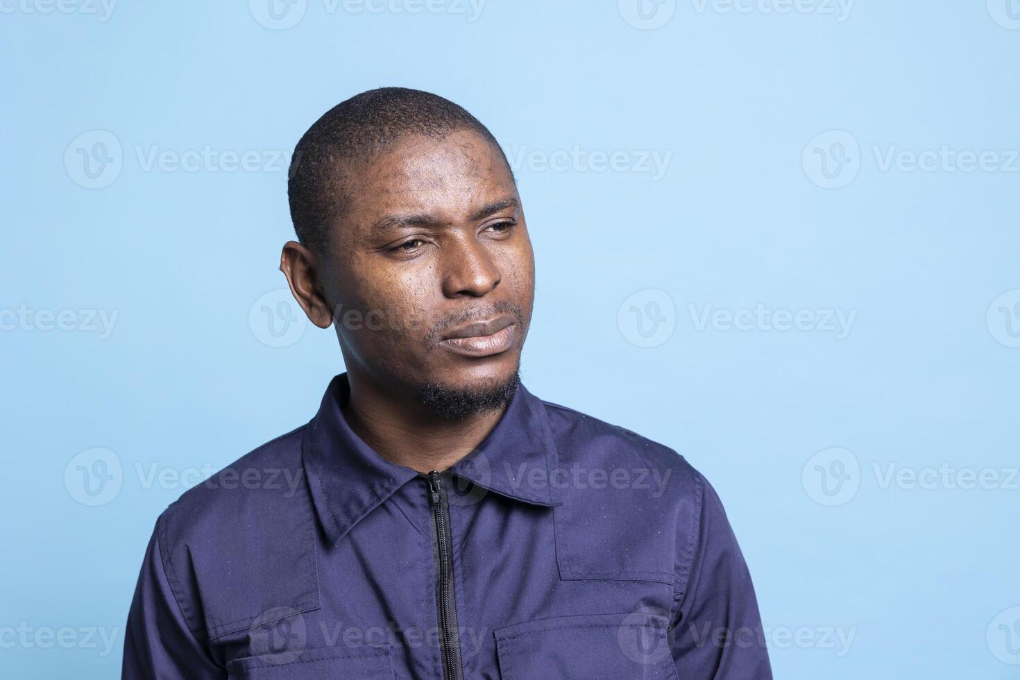 Young security officer posing in studio thinking of new safety measures, working on safeguarding the mall premises. Male skilled agent in professional uniform contemplates with alertness. photo