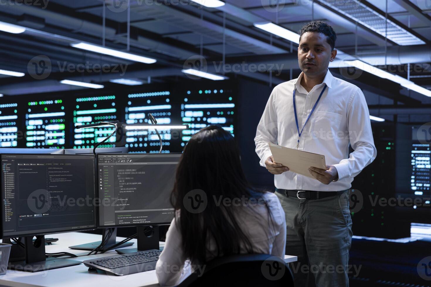 Data center inspector asks worker to show him emergency procedures paperwork, ensuring company is protected against system failure. Supervisor in server hub verifies industry regulations are respected photo