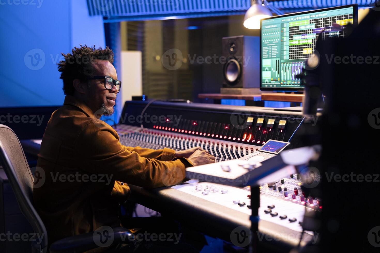 African american sound designer operating audio software to edit tracks and control panel board to mix and master the tunes. Professional music producer creating new songs, motorized faders. photo