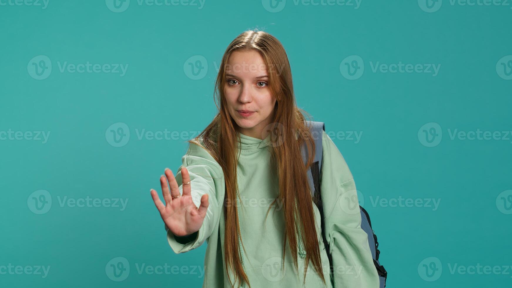 Assertive young woman doing stop hand gesture and talking. Annoyed girl doing firm halt sign gesturing, wishing to end concept, isolated over blue studio background, camera A photo