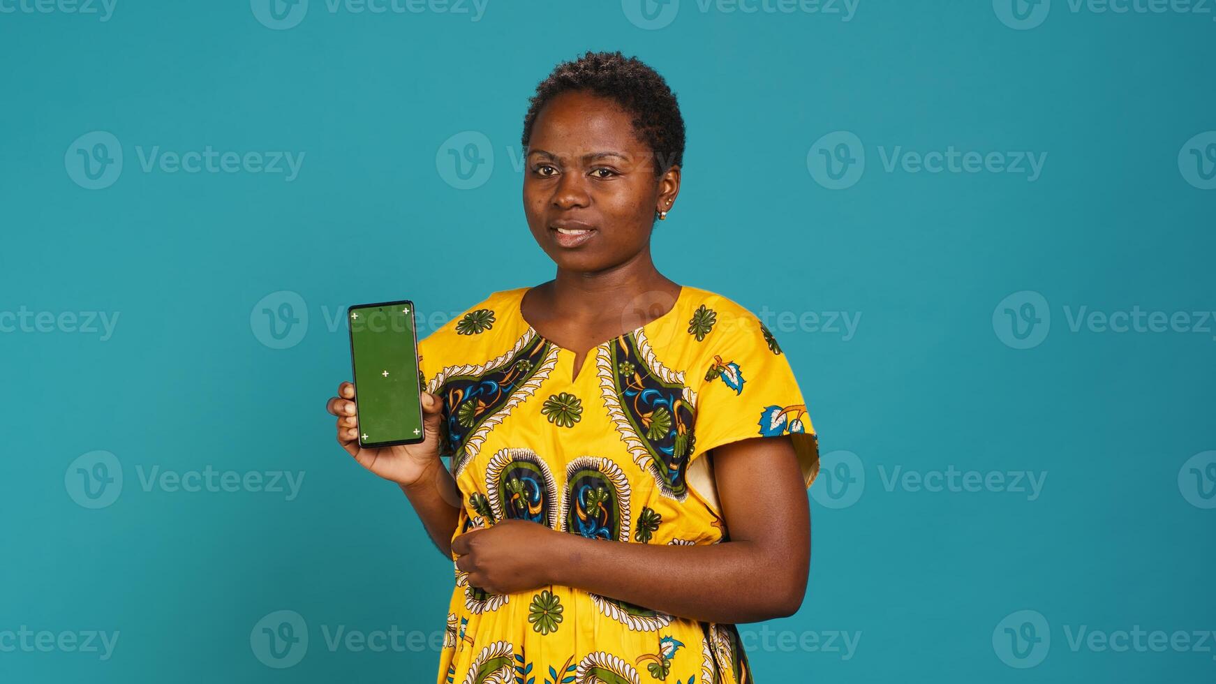Young confident woman presenting a green screen on smartphone, working in studio on an advertisement. Smiling natural girl holds a phone with isolated chroma key display. Camera A. photo