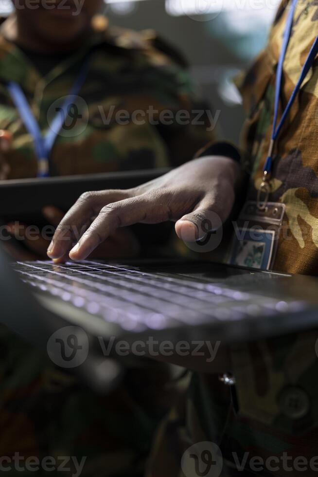 Army personnel operates on laptop to collect information from satellite footage, using world map projection to monitor activity. Gather intelligence for troops in the field. Close up. photo