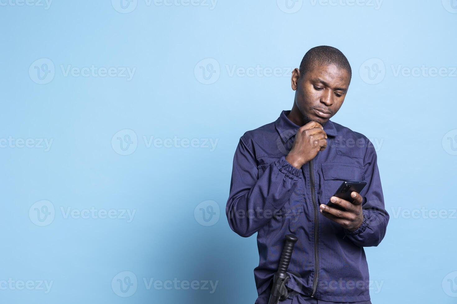 Patrol officer in uniform answering text messages on mobile phone, using social media apps to keep in touch with his friends during protection duty. Security guard checks online pages. photo