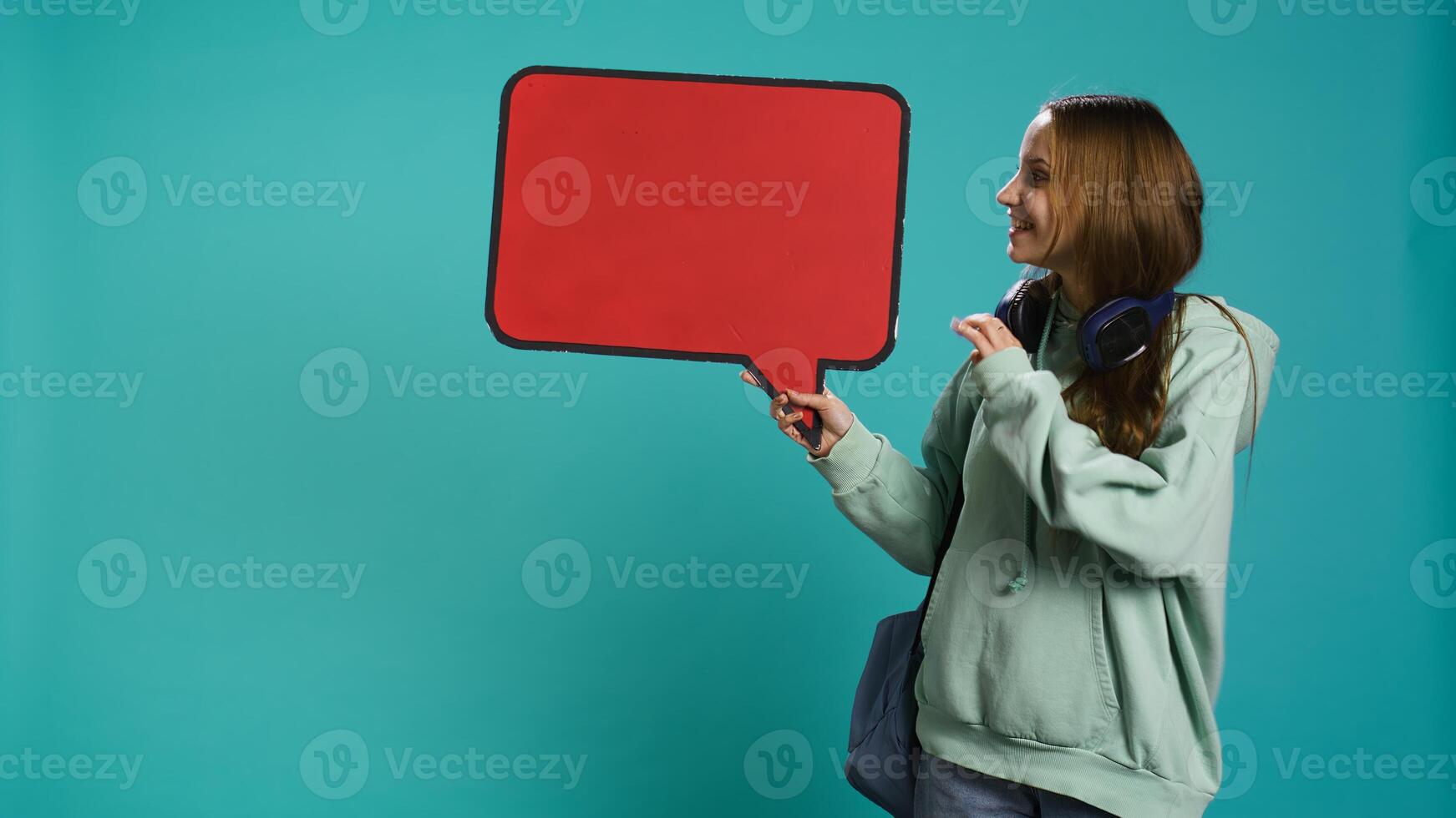Smiling woman holding red speech bubble sign of empty copy space for message. Joyous teenager presenting thought bubble cardboard used as promotion concept, isolated over studio background, camera B photo