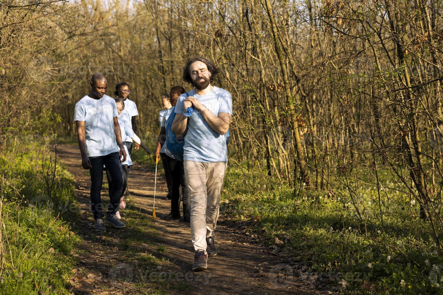 Pleased group of activists finishing litter cleanup in a forest area, grabbing their garbage disposal bags and going home. Happy team of people successfully cleaning the natural habitat. photo