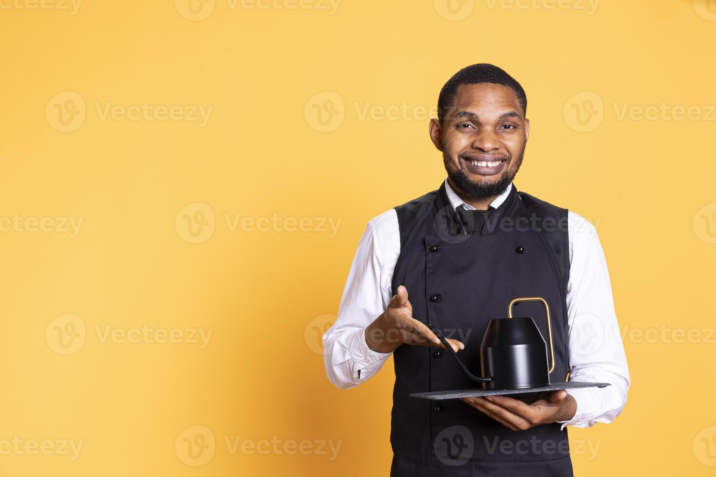 Skilled waiter bringing the teapot to the clients table to serve them tea before their meal order, service oriented industry. Employee with apron serves customers for satisfaction. photo