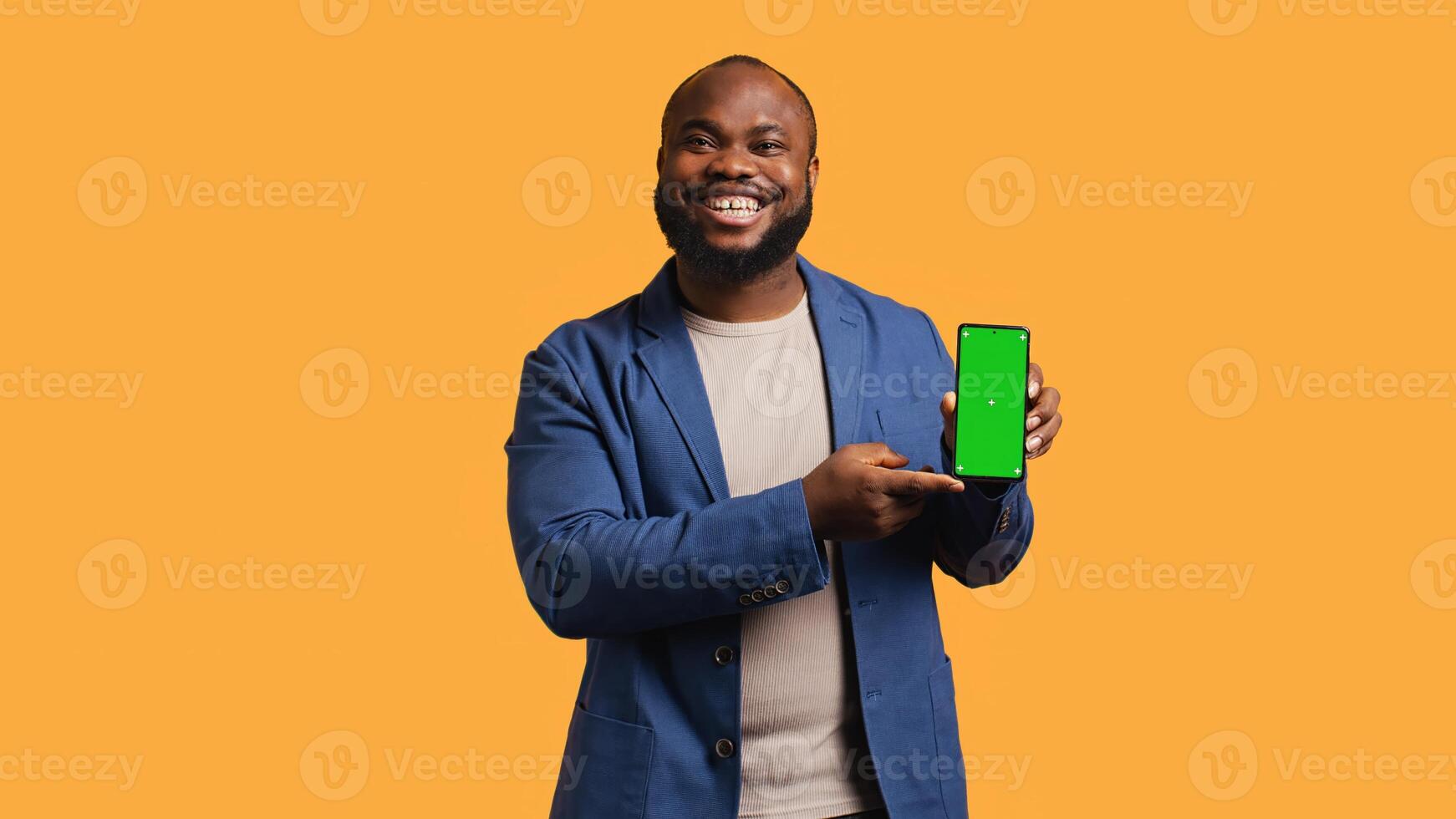 Smiling influencer presenting green screen mobile phone, isolated over studio background. Joyful BIPOC person holding copy space chroma key smartphone used for advertising brands, camera B photo
