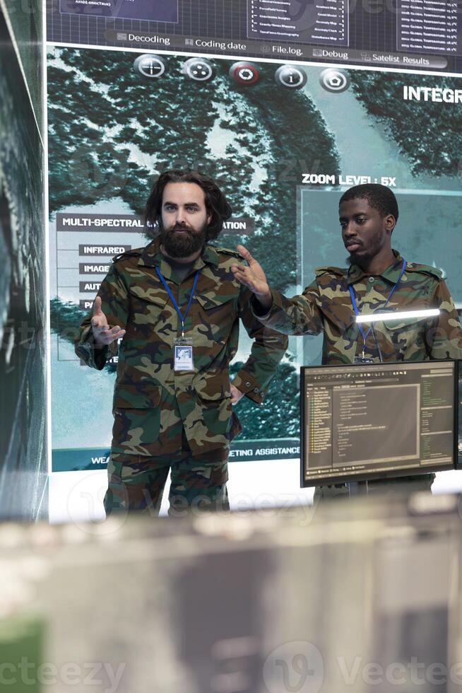 Professional army engineers gather intelligence for terrain operations, using surveillance CCTV footage in military power base. Soldiers examining important real time data on a big screen. photo