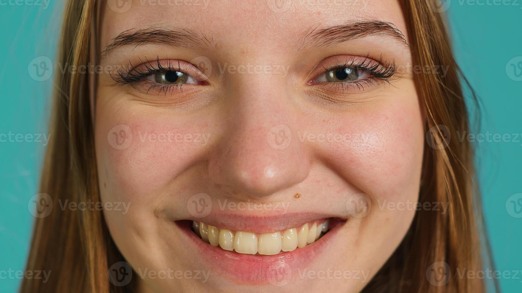 Extreme close up shot of elated joyful girl smiling, having fun, isolated over backdrop. Portrait of relaxed radiant woman grinning, having positive facial expression and good mood photo