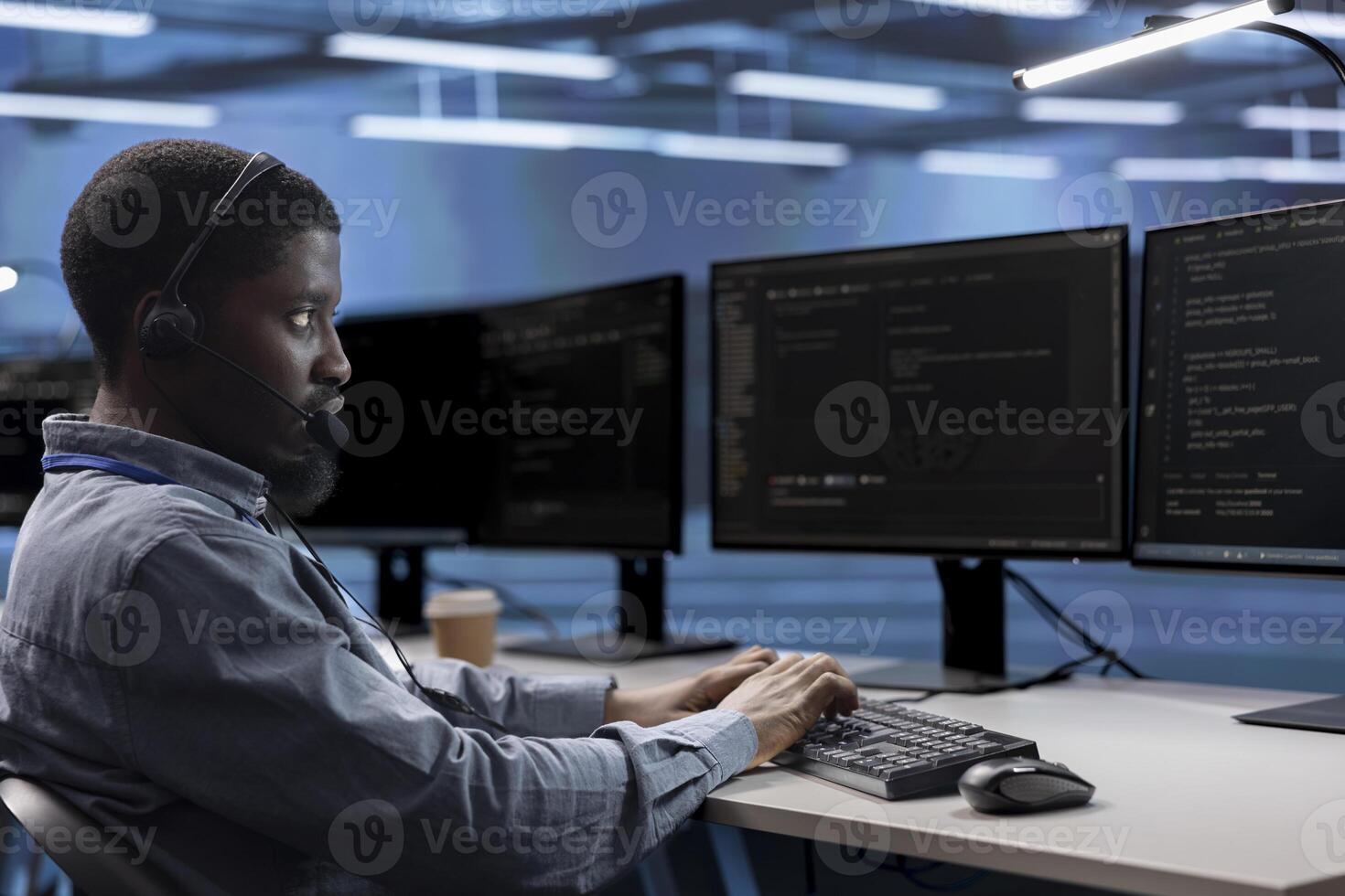 Engineer in data center managing call center tasks, speaking into headset while monitoring multiple computer screens. African american man talking with clients through headphones mic photo