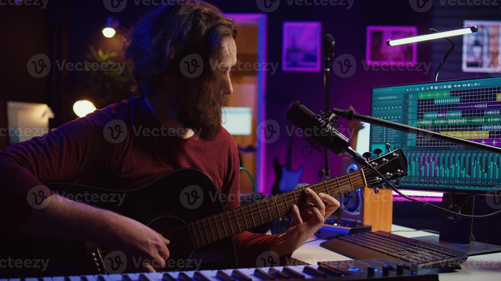 Artist composing a song with his acoustic guitar in home studio, recording notes and singing melody on microphone. Sound engineer mixing and mastering his tunes with stereo equipment. Camera B. photo