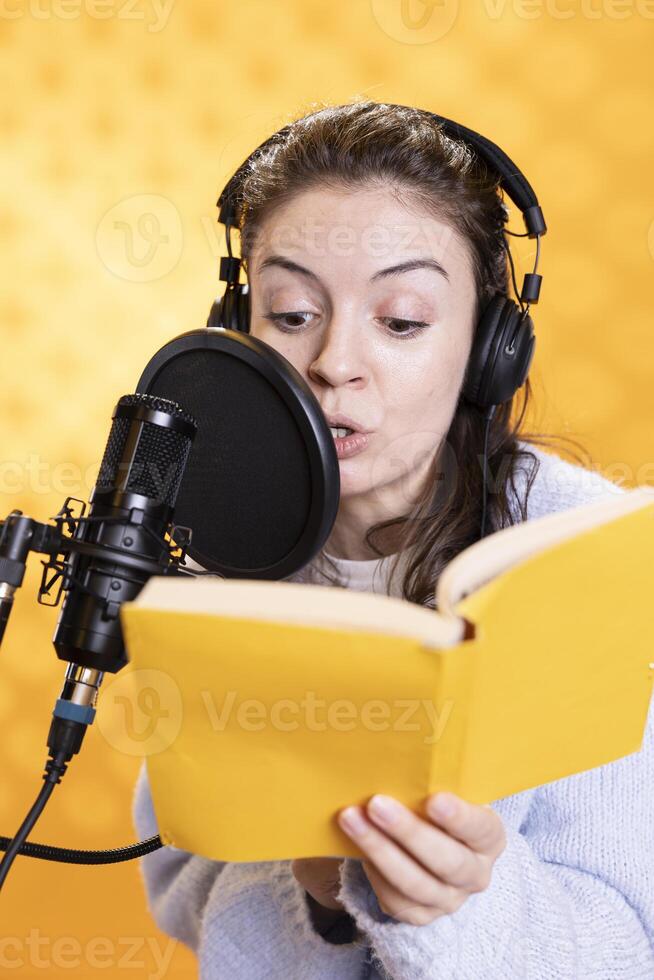 Woman doing voiceover reading of book to produce audiobook using dramatic acting. Narrator using storytelling skills and expressive sounds while producing recording of novel, studio background photo