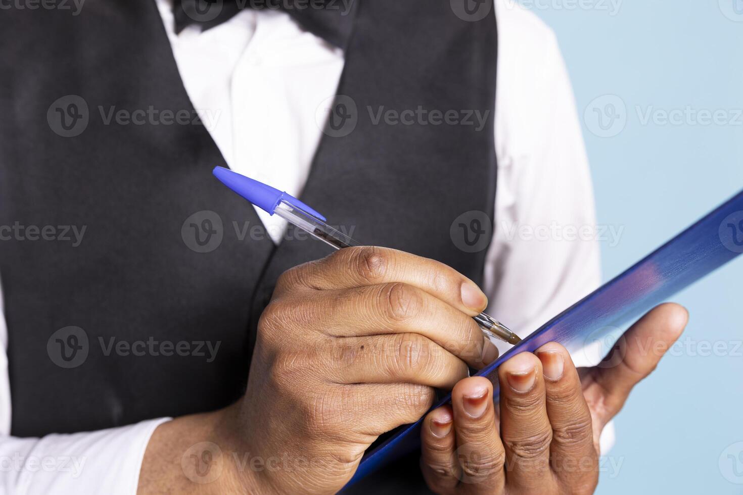 Receptionist bellboy takes notes on clipboard to offer great concierge services to clients, making a reservations list with all the hotel guests. Professional doorman in a tuxedo keeps account. photo