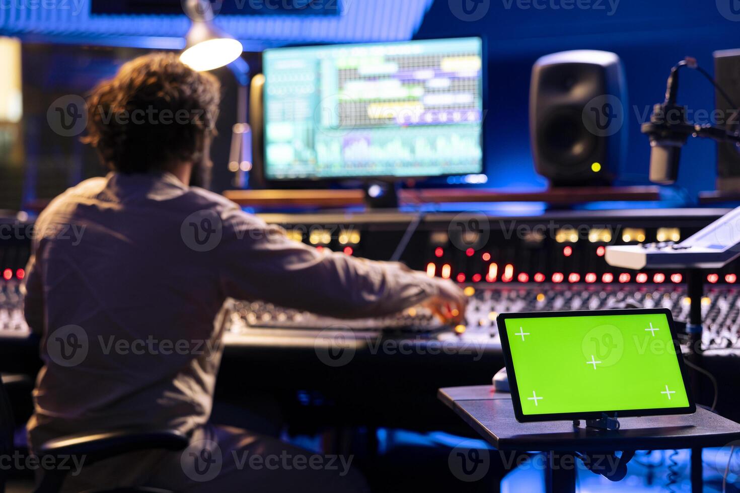 Tablet with isolated display in control room at professional recording studio, music producer editing and creating tracks for his new album. Sound designer works on mix and master with panel board. photo