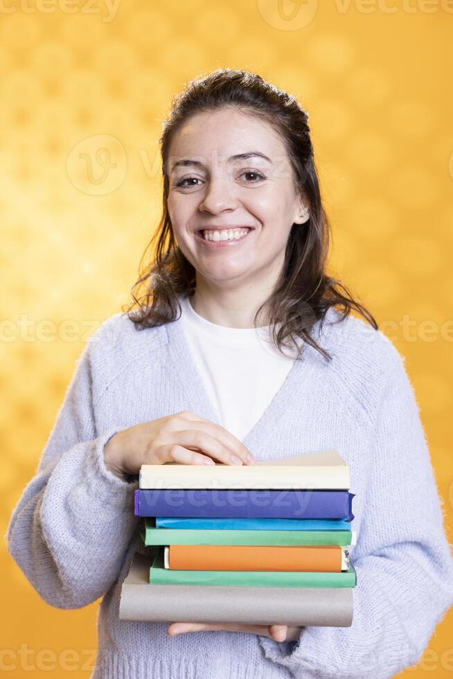 Portrait of joyous reading enthusiast woman holding stack of books, isolated over studio background. Cheerful nerd with pile of textbooks in arms used for academic learning photo