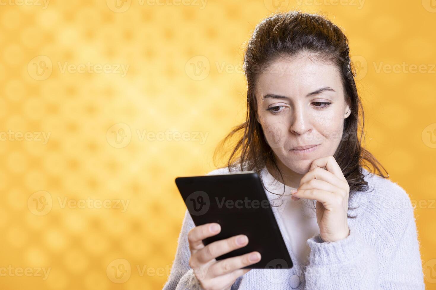 Woman reading captivating ebook on ereader device, enjoying hobby during leisure time. Bookaholic person with tablet in hands enjoying digital novel, scrolling on touchscreen, studio background photo