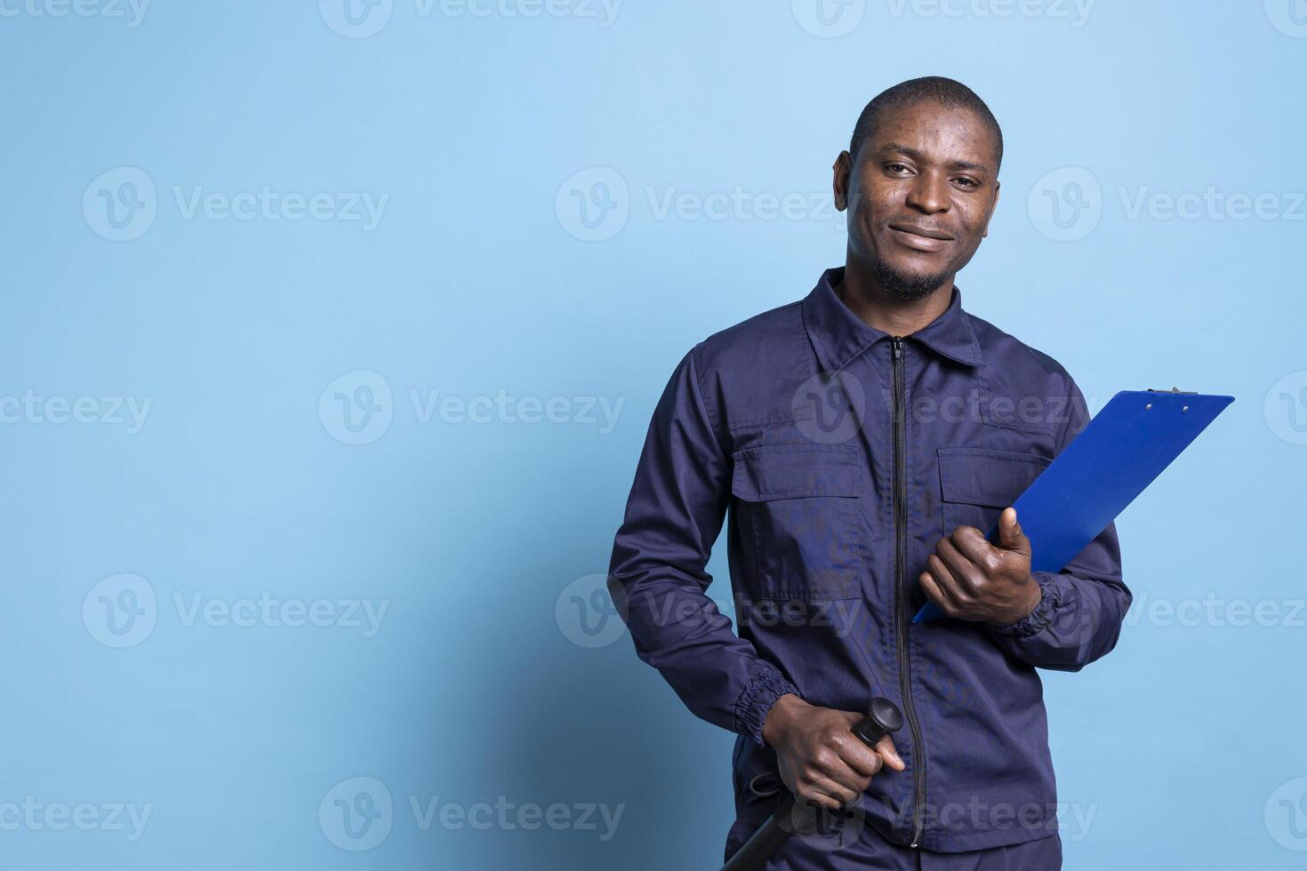 Security officer in uniform holding a checklist on papers and his baton, posing against blue background. Bodyguard keeping track of all the activities that are his responsibility, protection duty. photo