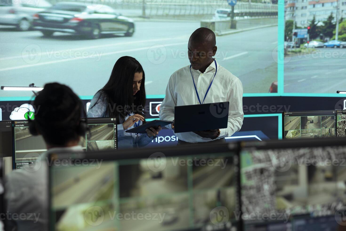 Indian woman working with her colleague to register a license plate number, monitoring traffic through CCTV surveillance radar system. Diverse agency employees oversee footage. photo
