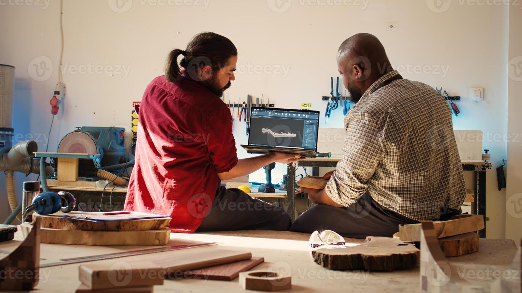 Woodworker looking over blueprints on laptop in CAD software with apprentice. Manufacturer and coworker designing custom 3D furniture on notebook in studio, preparing for customer order, camera B photo
