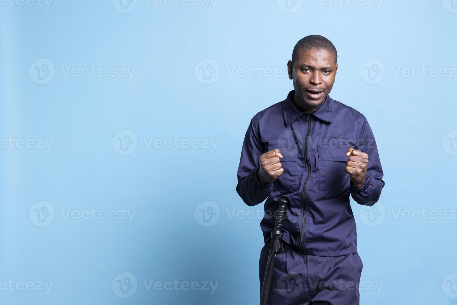 Enthusiastic happy african american agent being joyful about good news in studio, confident and optimistic security guard cheering against blue background. Spreading positivity. photo