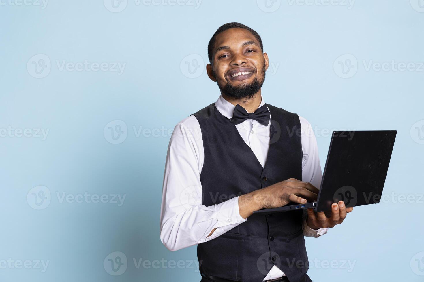 Bellhop employee making online remote reservations on laptop, browsing the hotel website to check lodging and availability. Doorkeeper staff gives assistance to guests. photo