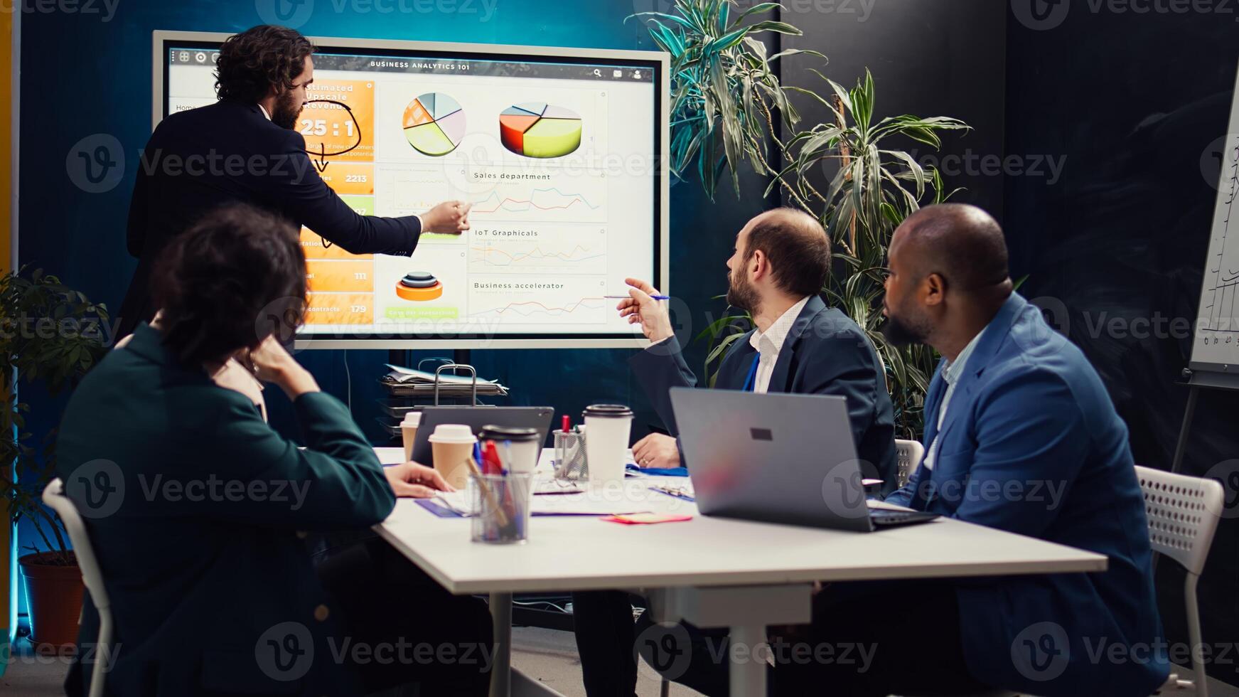 Project manager does a market research presentation for his team, better understanding of the situation. Associates work on technology or infrastructure investments to fulfill objectives. Camera B. photo