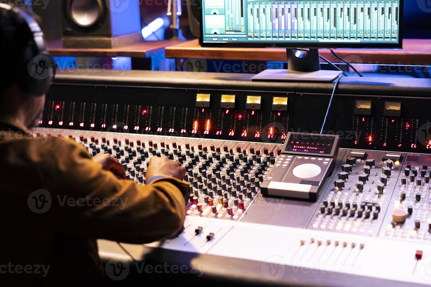 African american sound designer operates control room mixer and audio software for editing new music. Studio technician working with switchers, buttons, and volume level knobs, play hit song. photo