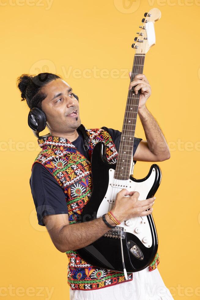 Joyful man holding electric guitar, playing rock music, isolated over studio background. Cheerful indian musician using musical instrument, doing concert, producing songs photo
