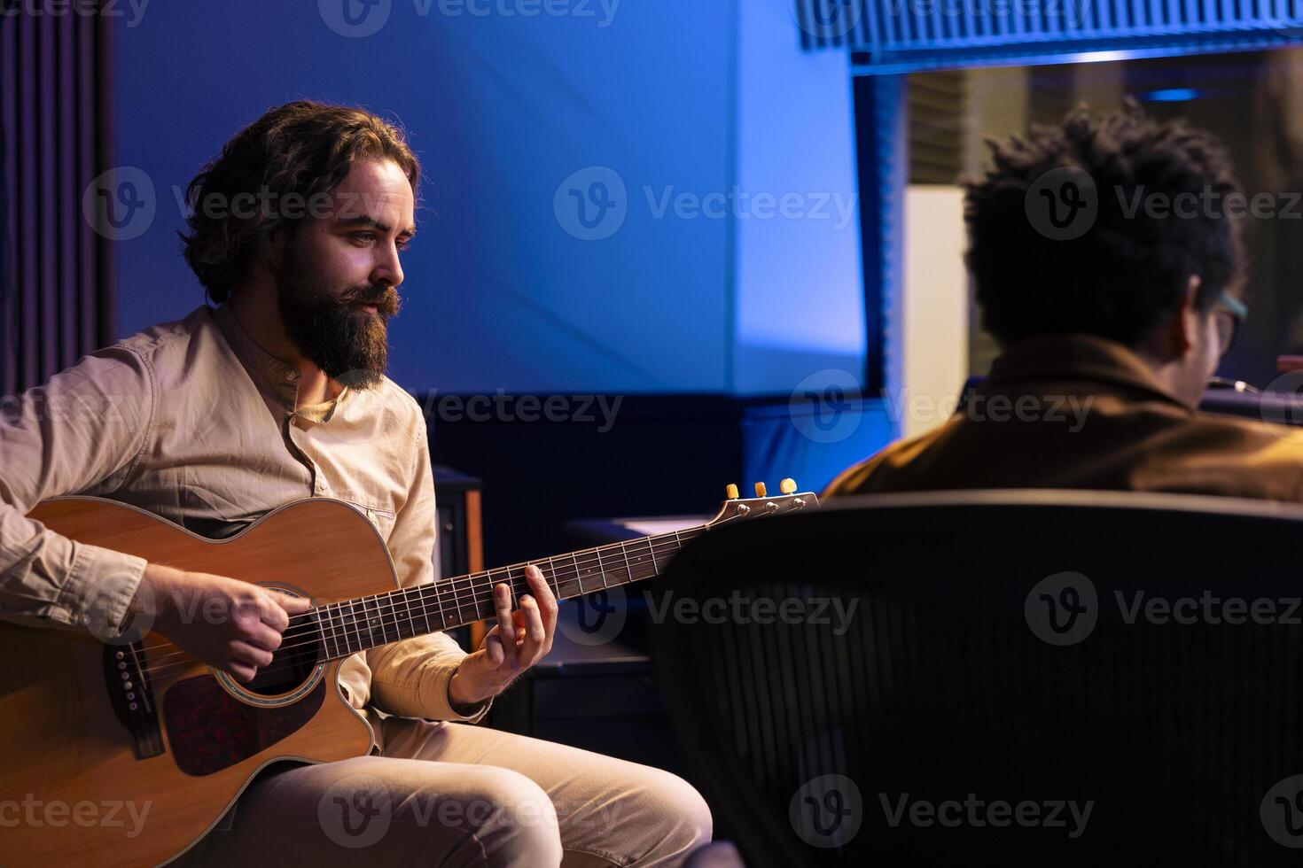 Artist recording his electro acoustic guitar tunes with producer in studio, doing mix and master to create a new hit song. Singer does live performance with musical instrument in control room. photo