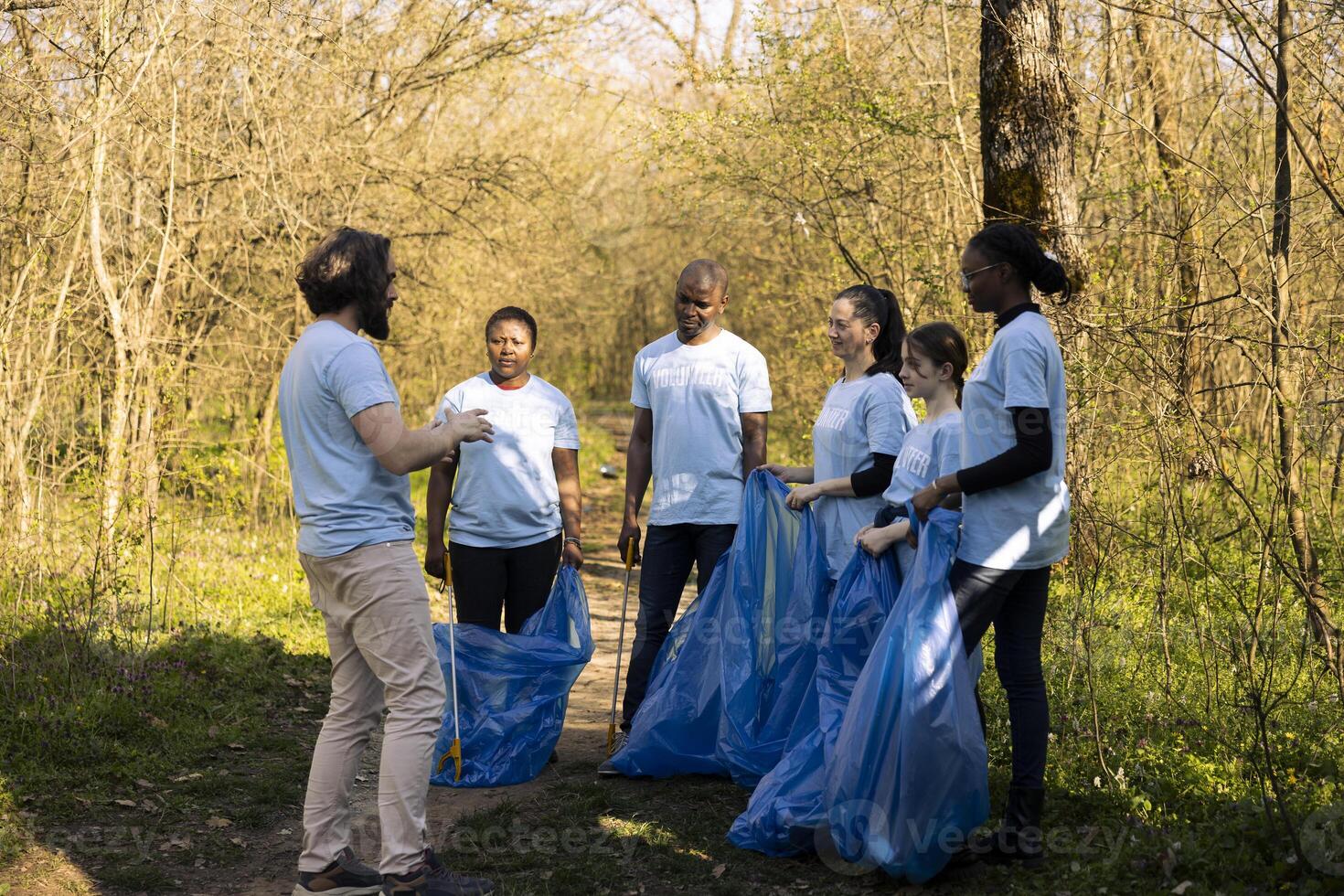 Group of environmentalists gathering to clean the forest area from junk, prepared with tools and garbage bags. Diverse people fighting pollution and illegal dumping, nature responsibility. photo