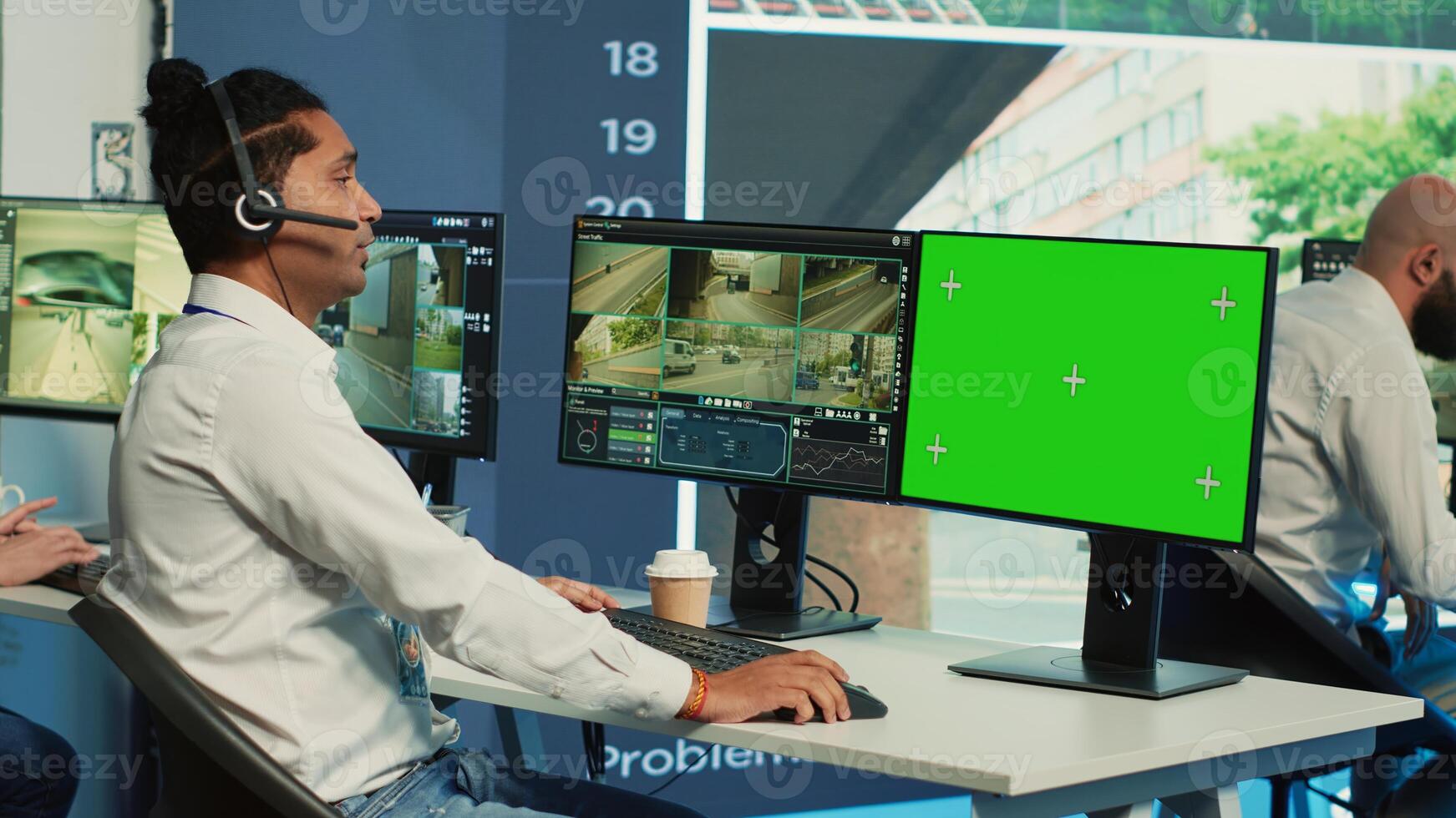 Indian operator monitors traffic next to a greenscreen on display, following surveillance footage from satellite radar cameras. Agency employee works with city CCTV system. Camera A. photo